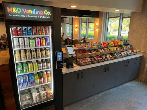 AI-generated concept rendering of a branded M & D smart cooler beside a tablet checkout and tiered snack shelves.